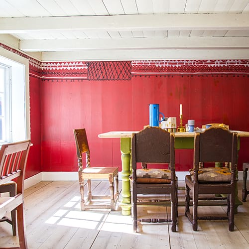 Kjøkkenet/eldhuset med grua, en kopi av en lokal peis, og et stort matskap som skjulte kjøleskapet. Skifergulvet er lagt av Ela og Henry.Det første besøkende møter er Elas naivistiske «kroting» i svart og hvitt.